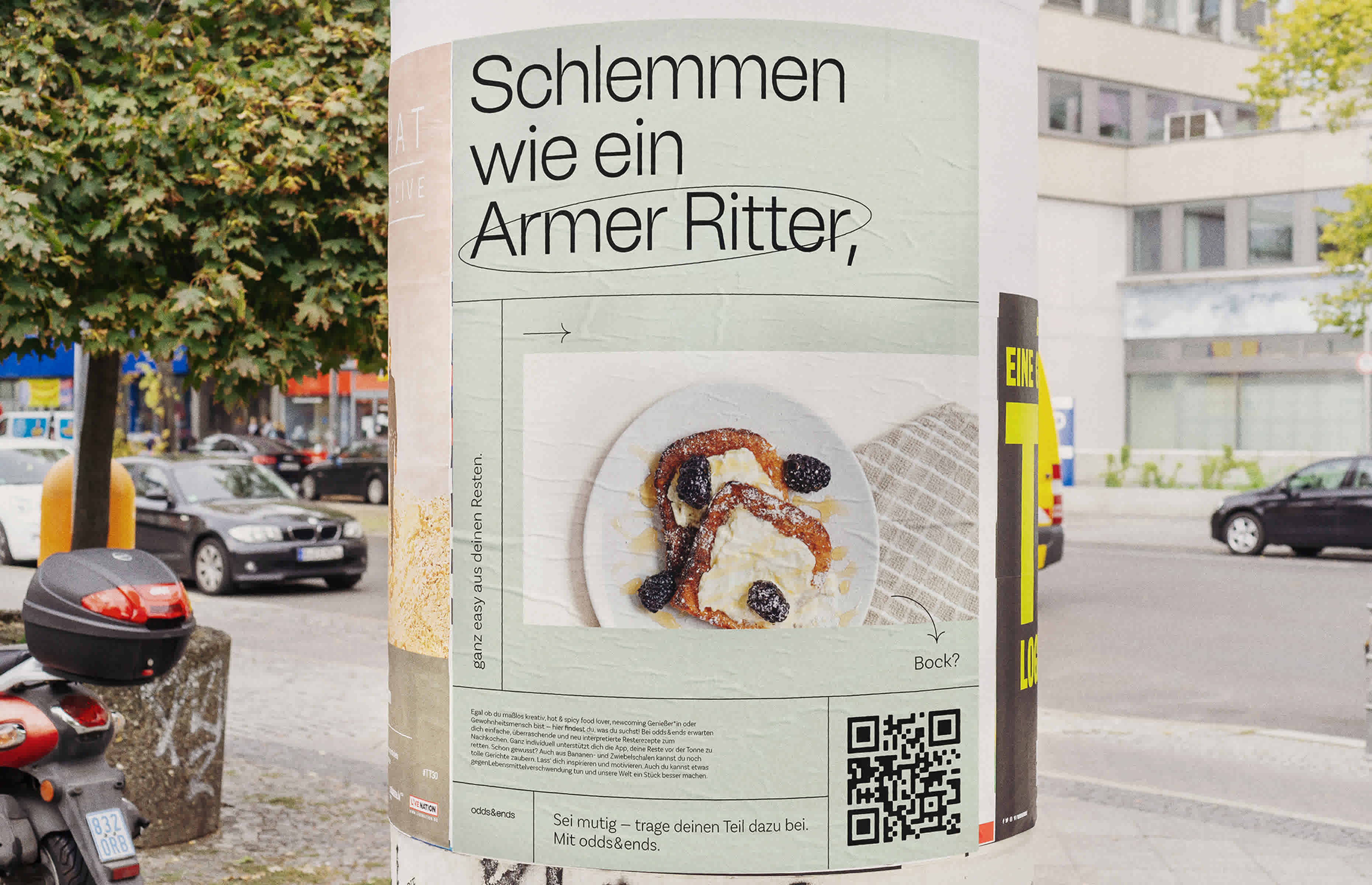 An einer Säule in einer belebten Umgebung mit Autos ist ein Plakat von der Kampagne odds & ends zu sehen. Es ist leicht grün und zeigt ein leckeres Gericht aus Resten.