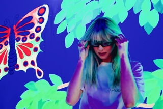 Portrait — woman with blue hair under neon butterfly light