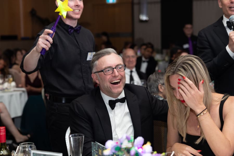 Guests laughing at their table as a volunteer holds up a glowing star wish wand