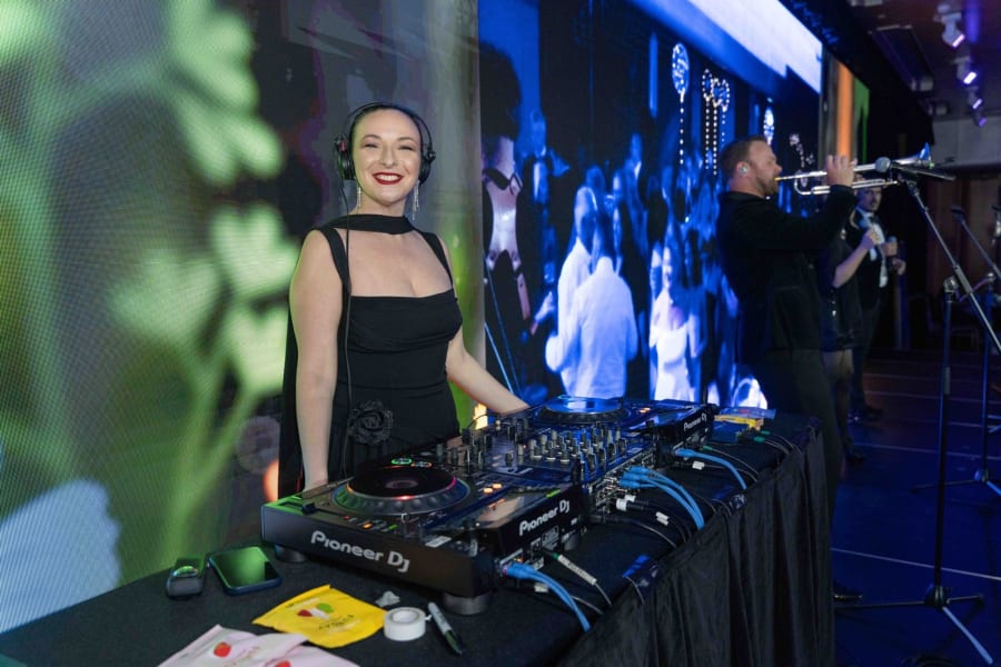 DJ smiling behind the decks with a trumpet player performing beside her