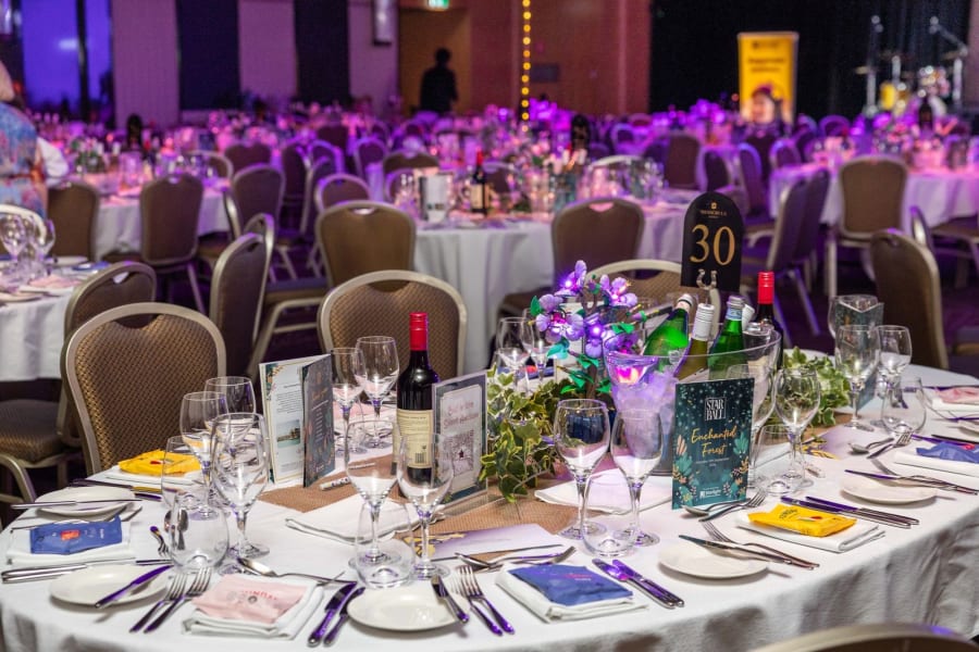 Illuminated floral table centrepiece with the full ballroom of guests behind at the Sydney Star Ball