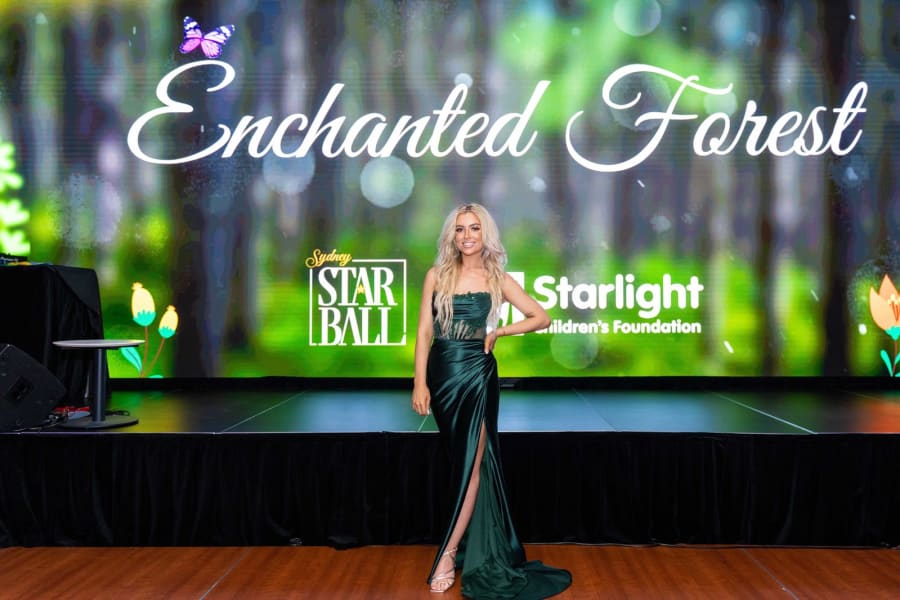 Guest in an emerald satin gown posing in front of the Enchanted Forest stage screen