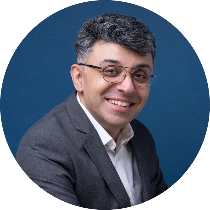 Corporate headshot of a smiling man in glasses and a charcoal suit, shown in the circular crop LinkedIn uses for profile photos