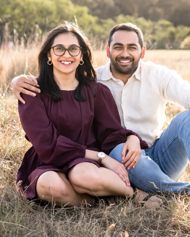 Engaged couple sitting together in golden grass at Rouse Hill Regional Park