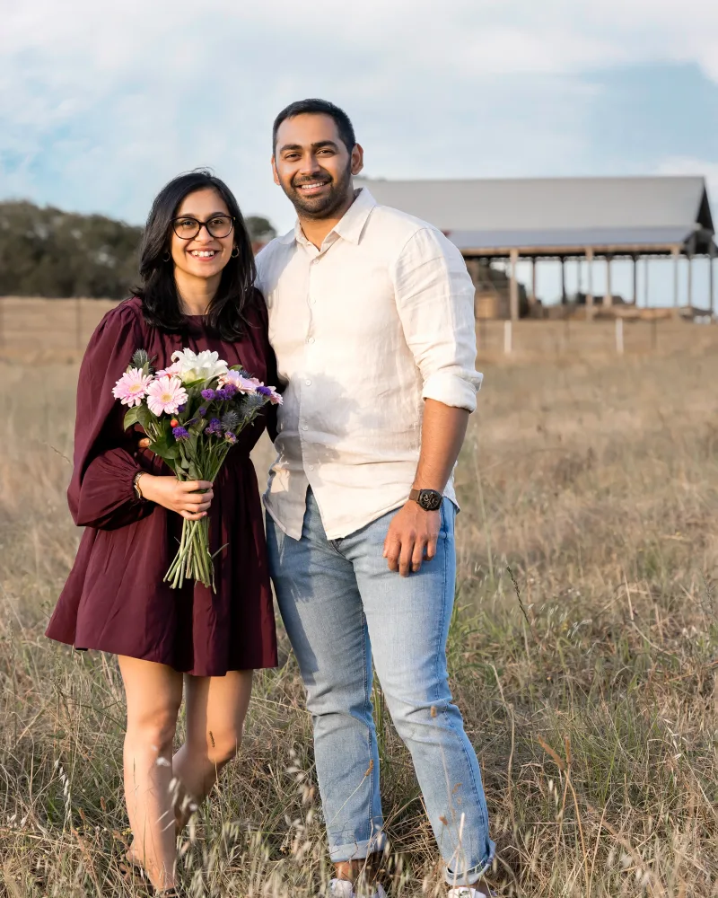 Engaged couple standing together holding a flower bouquet near a barn at Rouse Hill Regional Park
