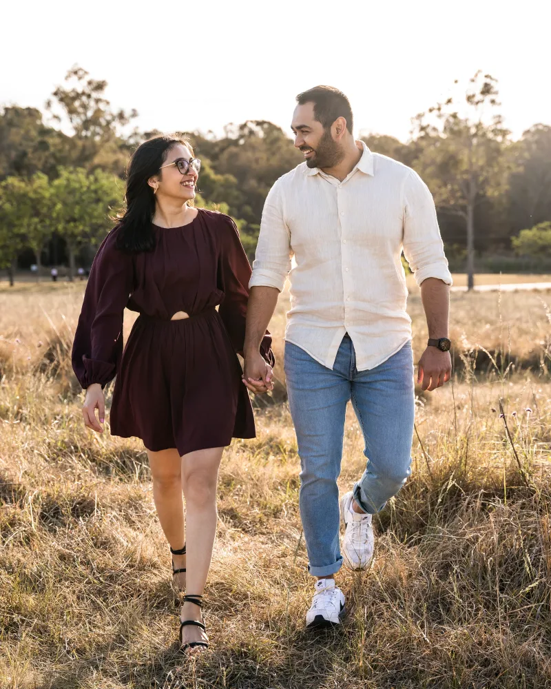 Engaged couple walking hand in hand through a grass field at Rouse Hill Regional Park