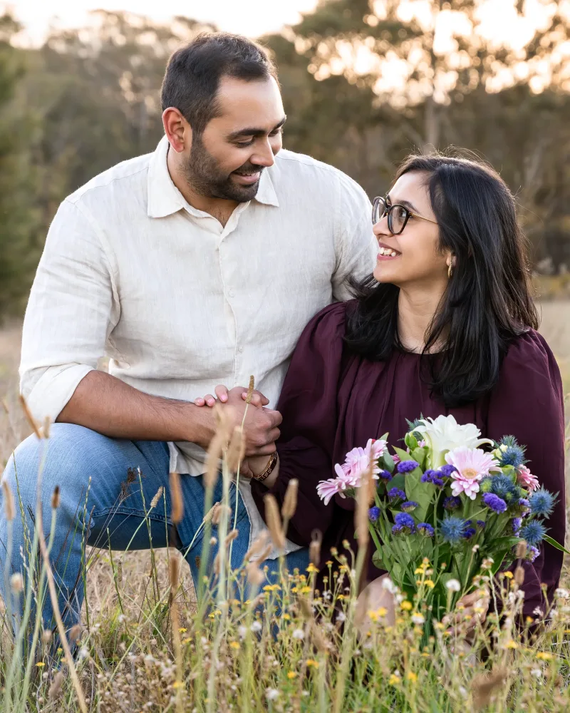 Engaged couple smiling closely at each other holding a flower bouquet at Rouse Hill Regional Park