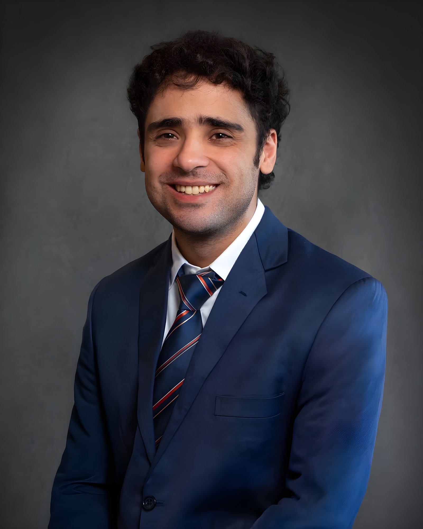 Corporate headshot of a young professional man in a blue suit and striped tie