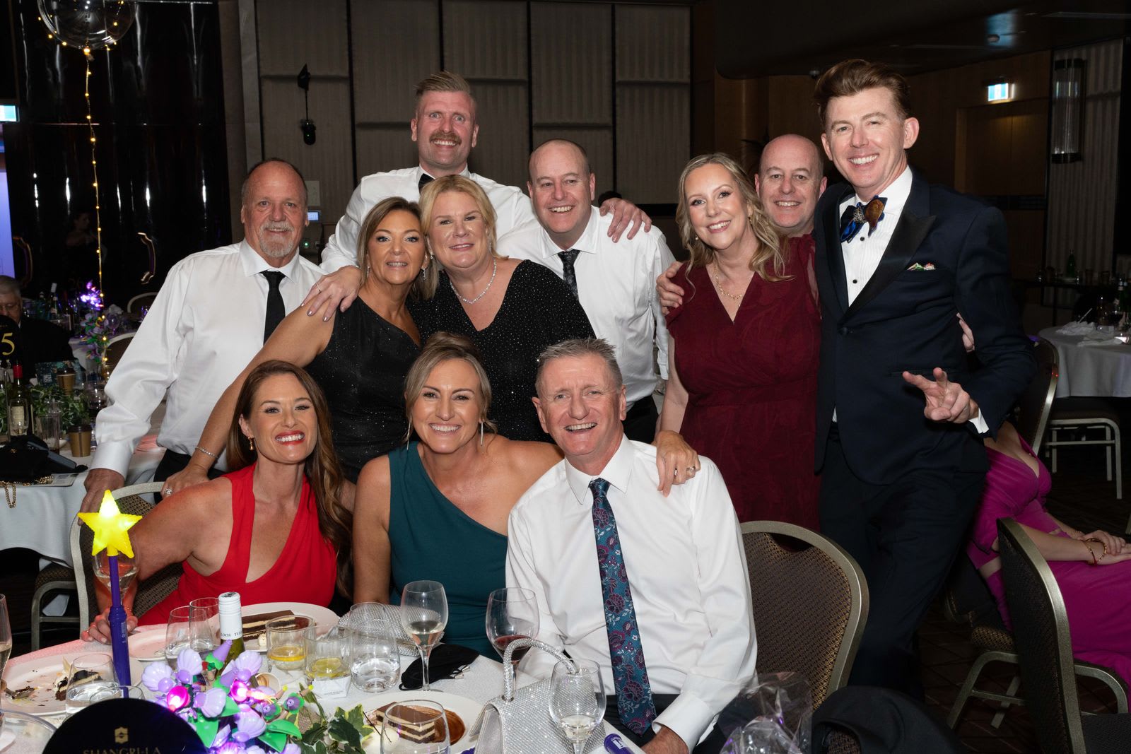 Group of ten smiling guests posing together at their dinner table during a corporate gala in Sydney