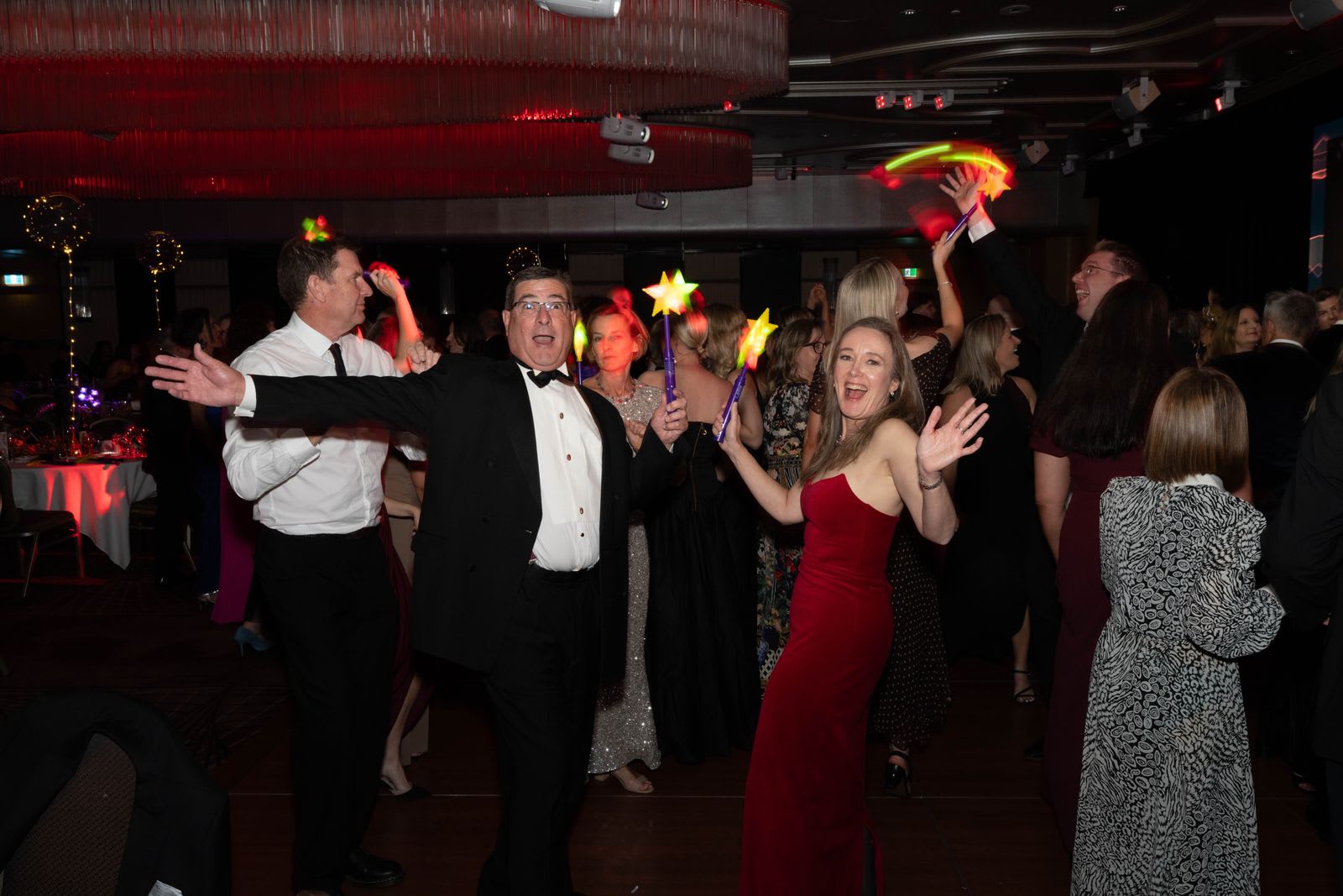 Guests dancing with glowing star wands under a red-lit chandelier on the dance floor at a Sydney charity gala