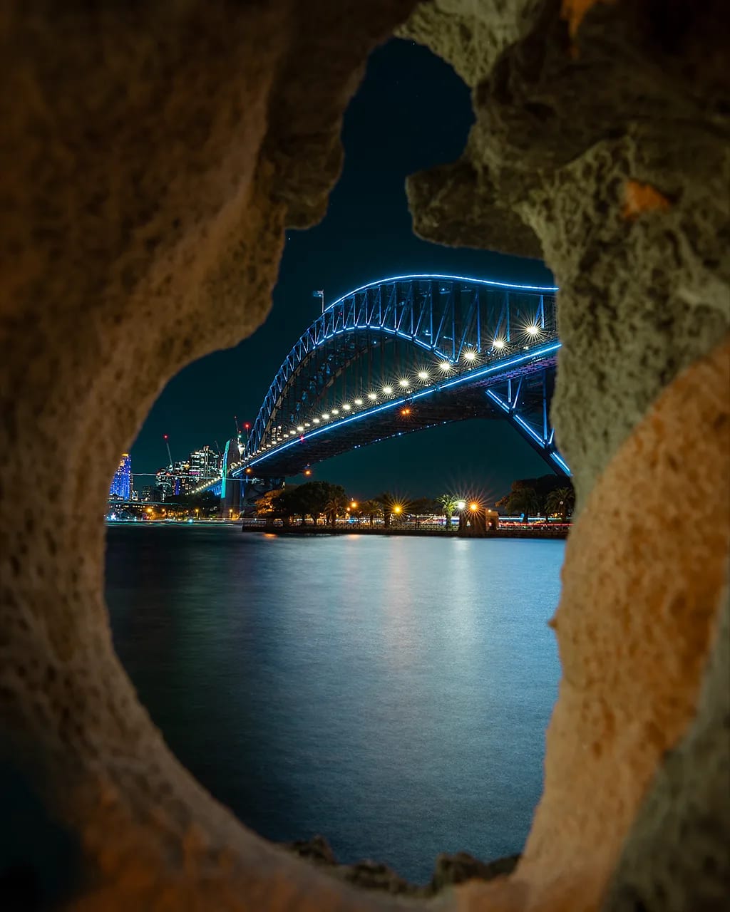 Sydney Harbour Bridge at night — vivid lights through rock hole by Shekhar Jay Photography