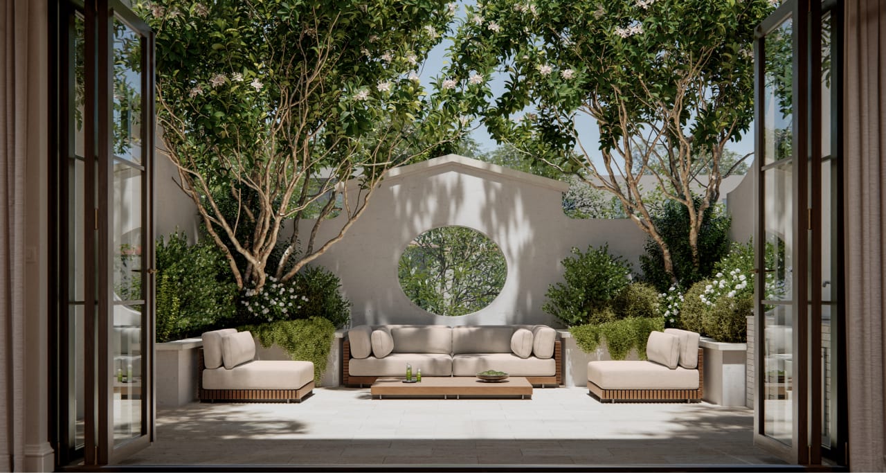 Expansive private courtyard at The George viewed through open bi-fold doors, with mature trees, lush tropical plantings, a carved circular garden feature, and modular ivory seating beneath dappled light