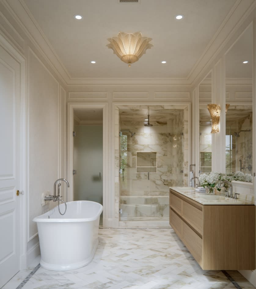 Primary bathroom at The George with a freestanding soaking tub, natural travertine floors, Italian wood vanity, and Waterworks fixtures set against soft neutral stone walls