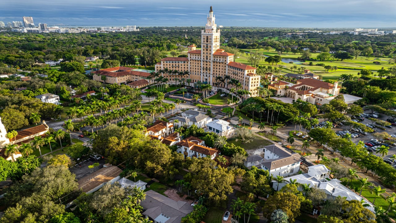 Aerial panorama of Coral Gables featuring the landmark Biltmore Hotel, lush tree canopies, and the surrounding neighborhood where The George is situated