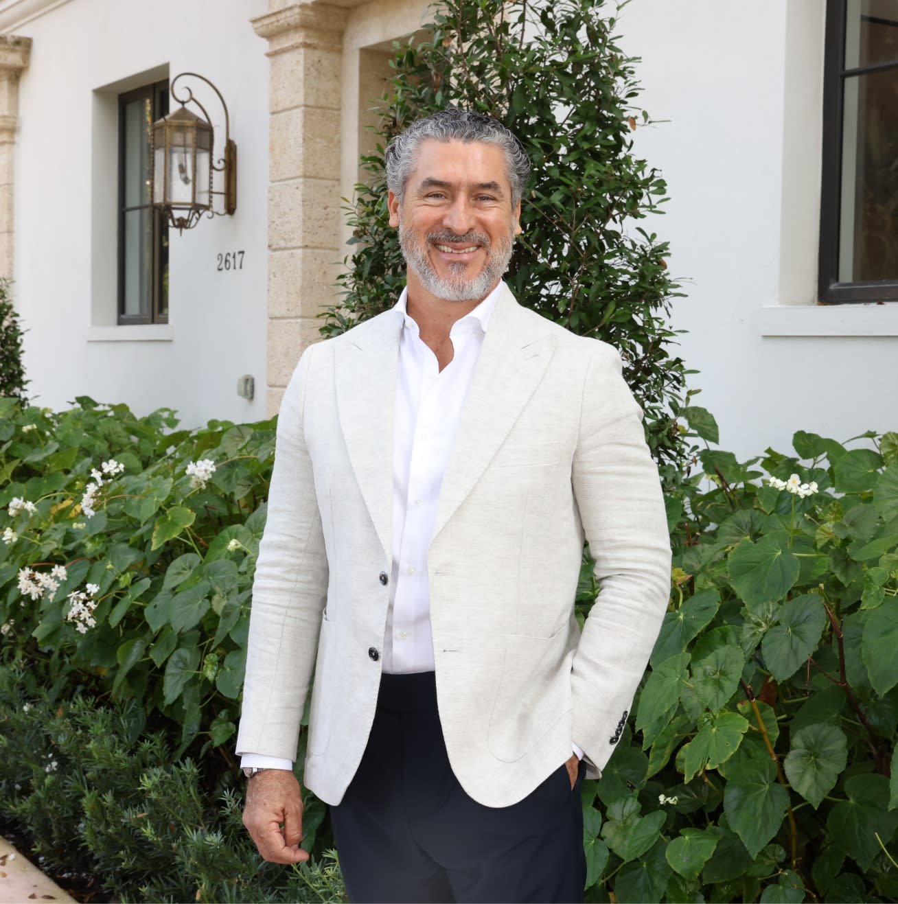 Alirio Torrealba, founder and CEO of MG Developer, photographed outdoors in a white blazer against a backdrop of tropical greenery