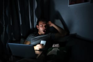 Man sitting with a phone screen and computer getting tired