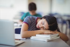 Tired schoolgirl sleeping in classroom at school