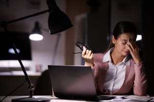 Young businesswoman touching her head while sitting at her workplace with laptop she tired of her work at office