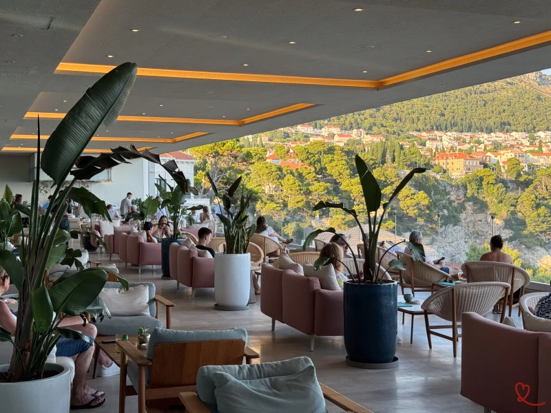 Interior de una moderna cafetería con clientes sentados y vistas a verdes colinas.