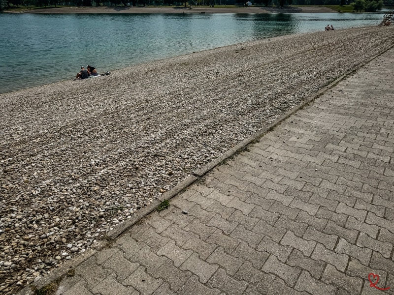 Playa de guijarros a orillas del lago Jarun con gente sentada.