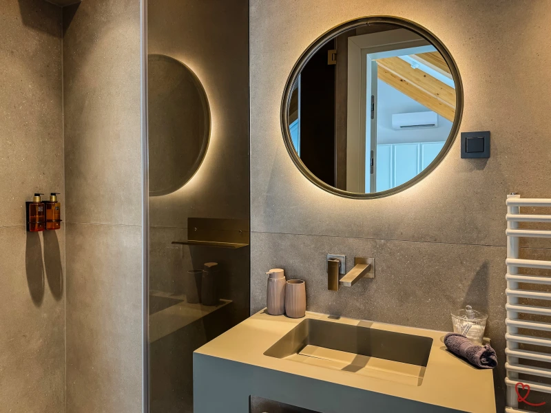 Salle de bain moderne avec lavabo, miroir rond et accessoires en verre.