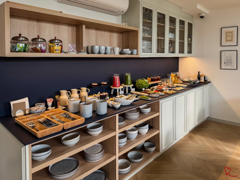 Buffet de petit-déjeuner avec plats, couverts et boissons sur un comptoir en bois.