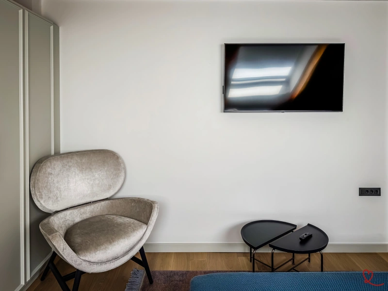 Fauteuil gris à côté d'une table basse et d'une télévision murale.