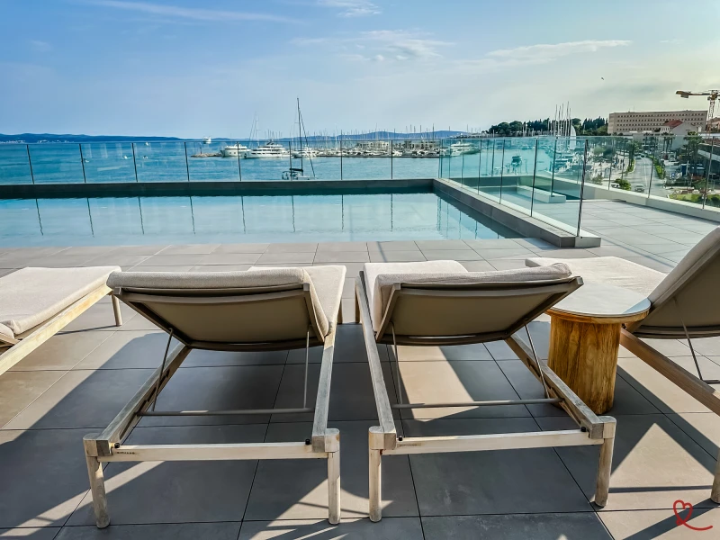 Espreguiçadeiras junto à piscina com vista para o mar e para o porto.