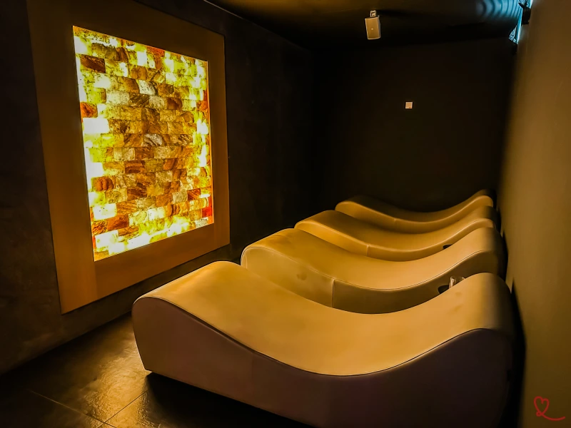 Espreguiçadeiras numa sala escura com uma parede luminosa de pedra salgada.
