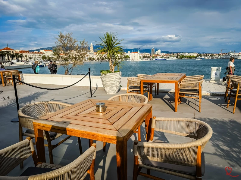 Esplanada-cafetaria com mesas de madeira e vista para o mar e para a cidade.