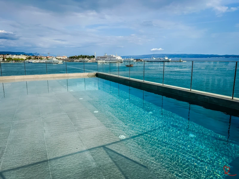 Vista de uma piscina no telhado com uma paisagem marítima em fundo.