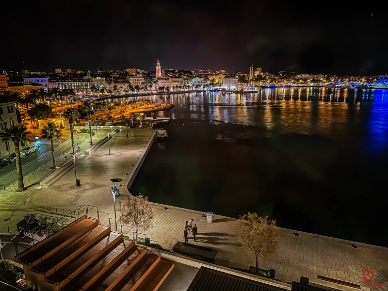 Vista nocturna de um porto movimentado com luzes reflectidas na água.