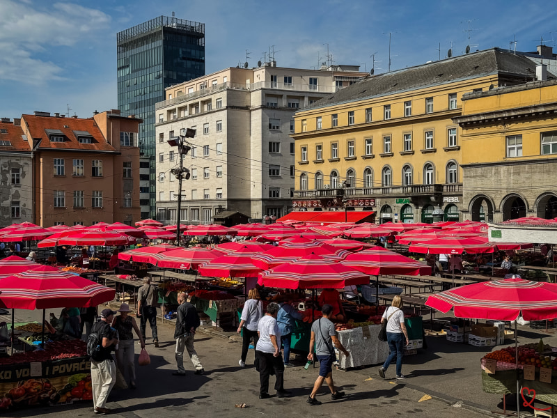 Marché animé avec des stands sous des parasols rouges et des visiteurs.