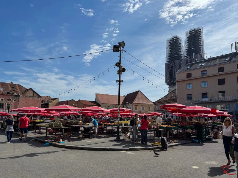 Marché en plein air avec des stands sous des parasols rouges et des visiteurs.