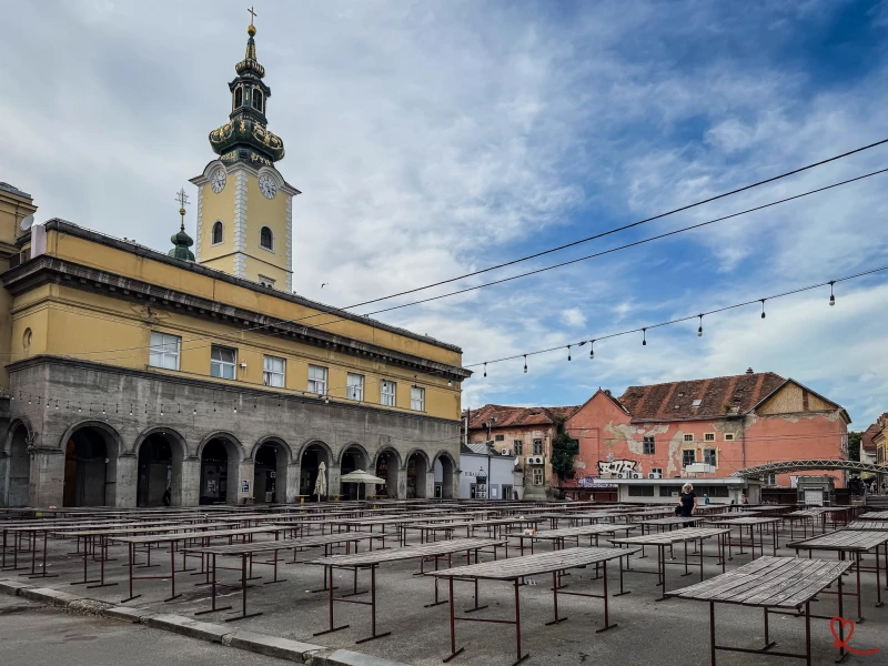 Place vide avec des tables en bois et une horloge sur un bâtiment historique.