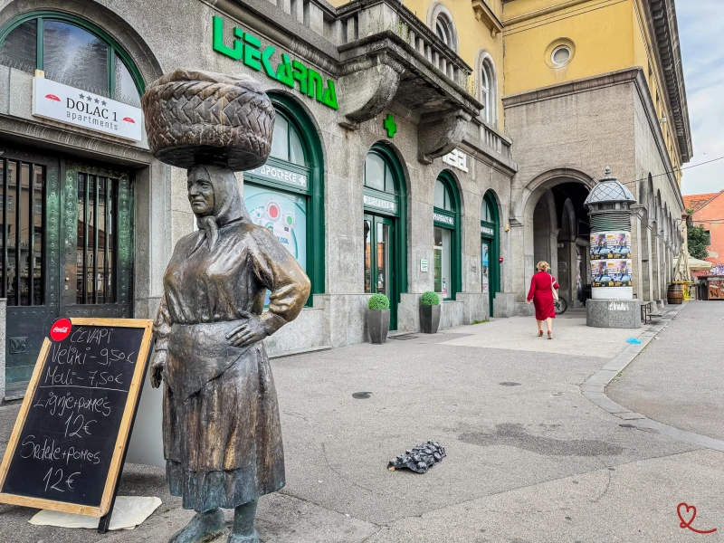 Femme en statue portant un grand panier sur la tête devant un magasin.