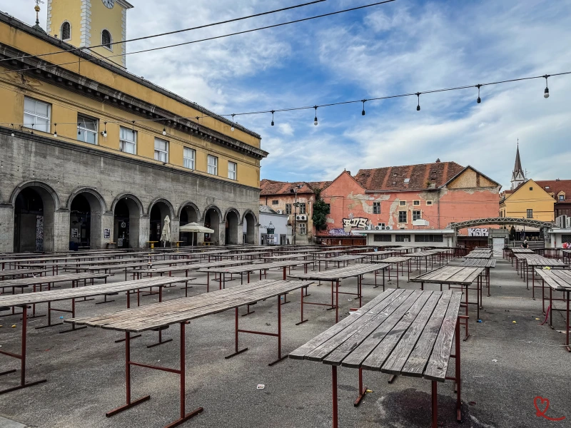 Place vide avec des tables en bois et des bâtiments colorés en arrière-plan.