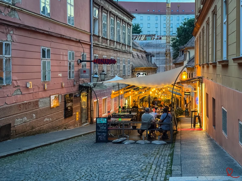 Rue pavée avec des tables de restaurant sous une toile, éclairage doux en soirée.