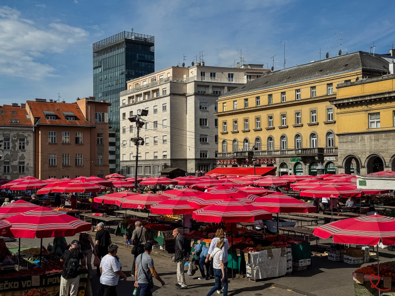 Marché en plein air avec des parasols rouges et des visiteurs entre les étals.