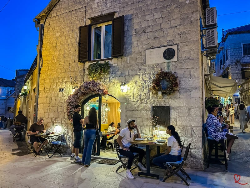Groupe de personnes dînant en extérieur devant un restaurant en pierre.