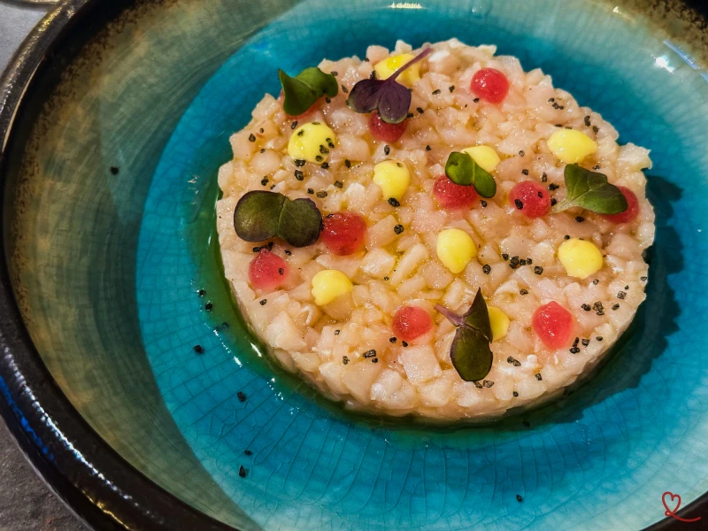Tartare d'espadon avec des garnitures colorées sur une assiette bleue.