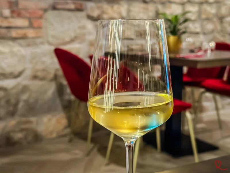 Verre de vin blanc posé sur une table avec des chaises rouges en arrière-plan.