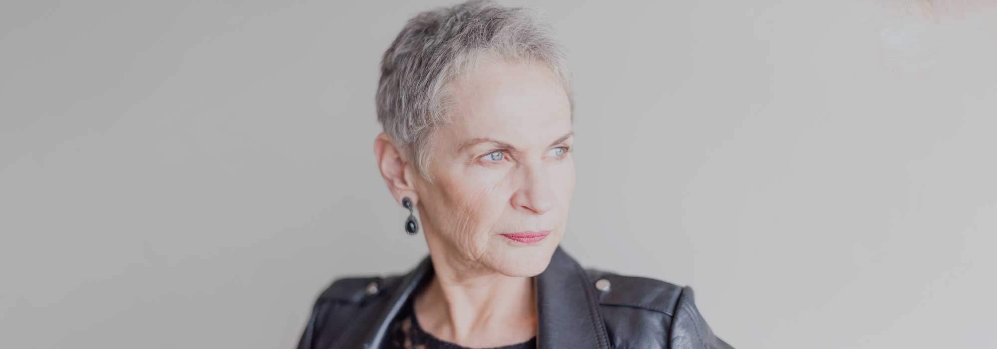 Senior woman with short grey hair, wearing a black leather jacket, she's looking pensive