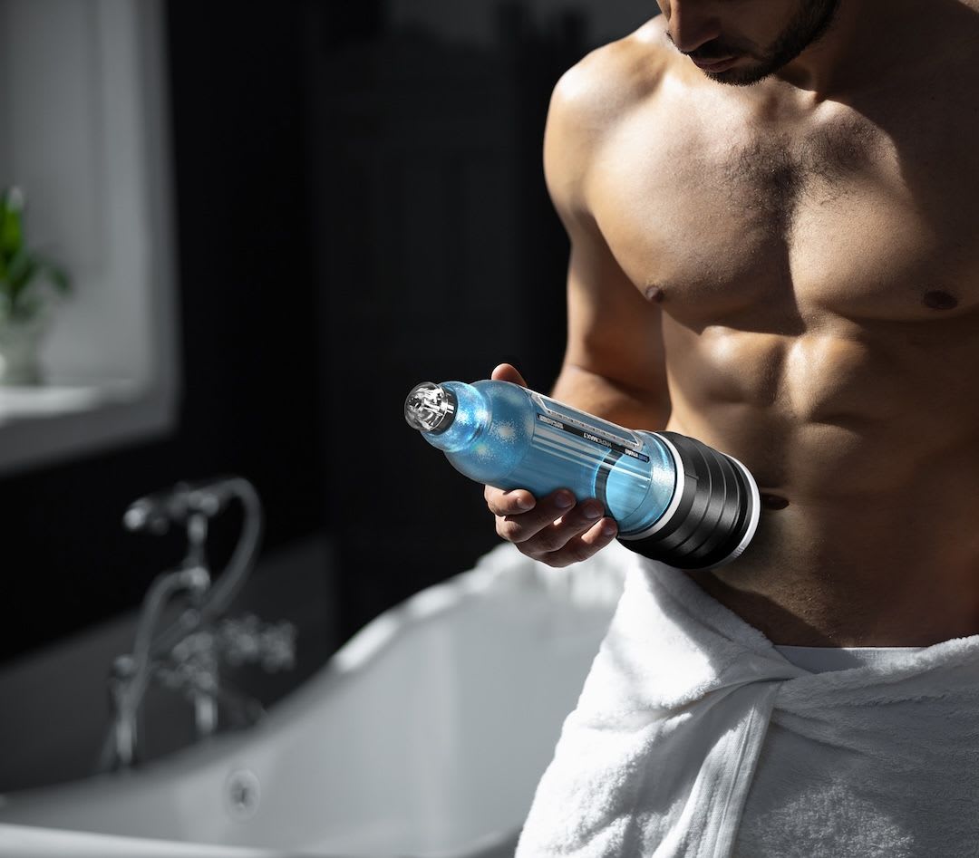 Topless man wearing a white towel around his waist and holding the Bathmate penis pump