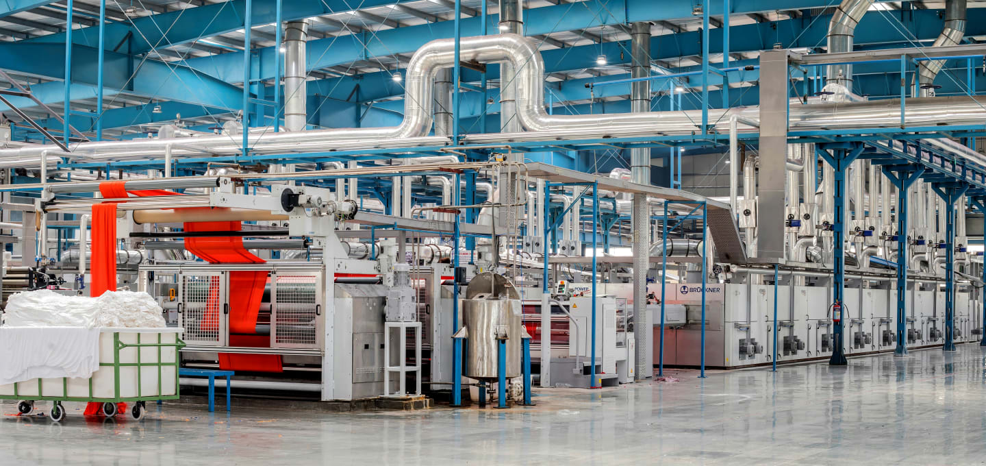 Interno di uno stabilimento industriale con linea di macchinari e tubazioni per la lavorazione tessile