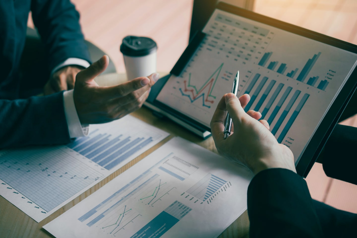 Due professionisti analizzano grafici finanziari su un tablet e report cartacei durante una riunione