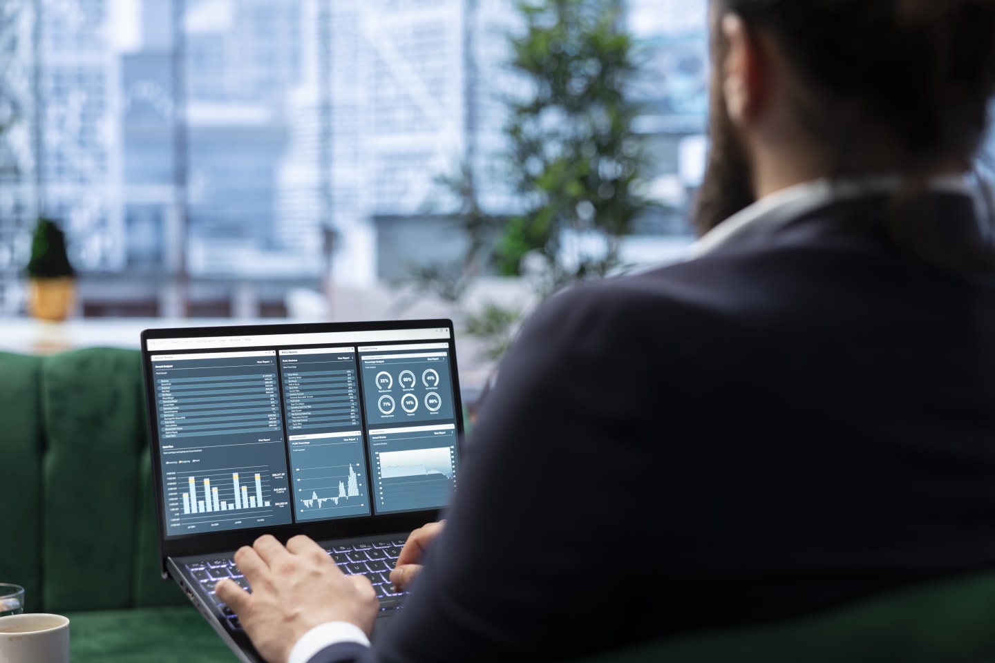 Un professionista consulta una dashboard di indicatori sul laptop davanti a una vetrata sulla città