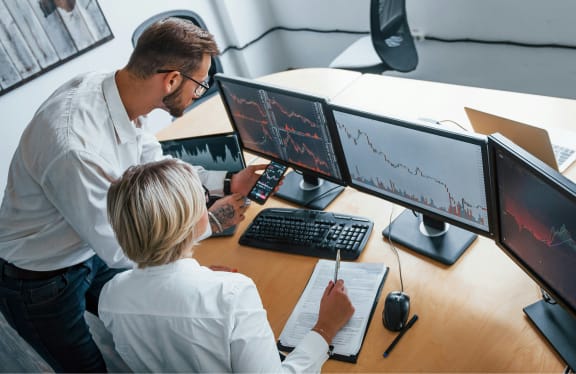 Due professionisti analizzano grafici finanziari su più monitor in un ufficio