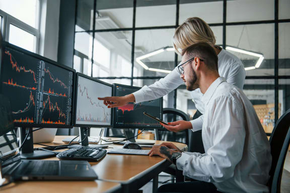 Due analisti osservano grafici finanziari su più schermi in un ufficio luminoso