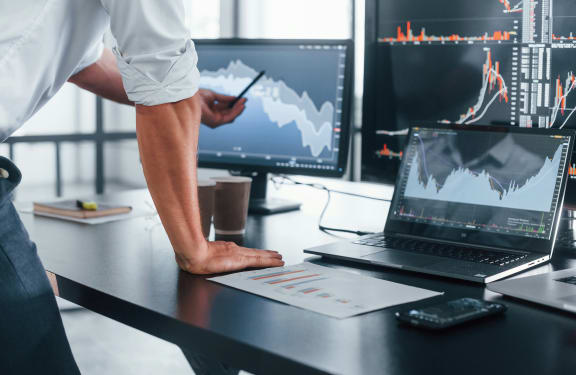 Professionista analizza grafici e dati finanziari su monitor e laptop in ufficio